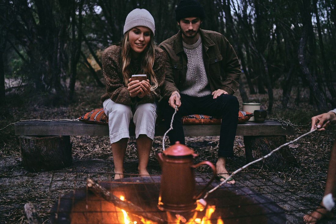 A copper kettle heating over an open campfire in the bush at dusk