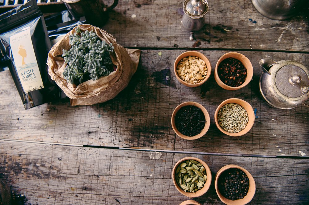 Loose leaf tea and whole spices in terracotta bowls on a weathered timber bench