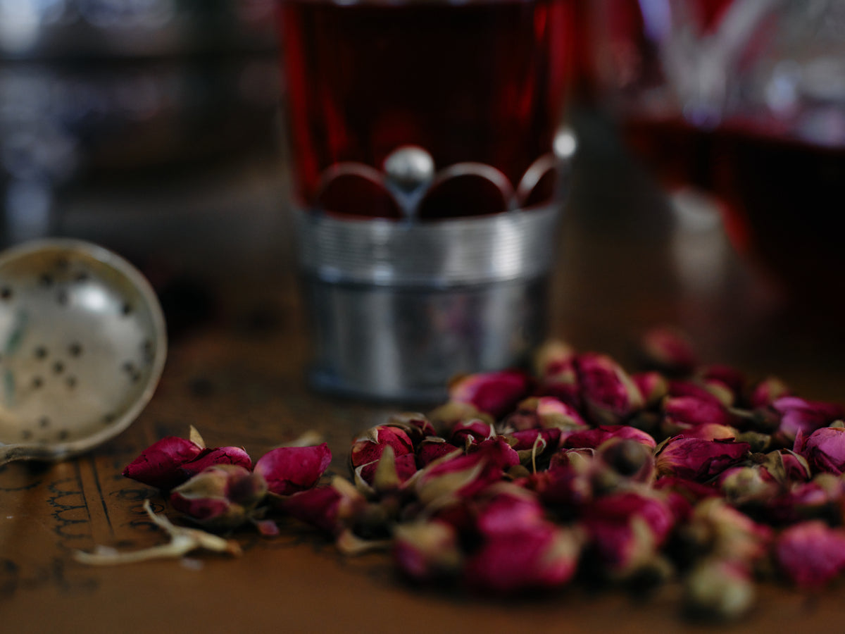 Dried rose buds scattered on a brass tray beside a silver tea strainer